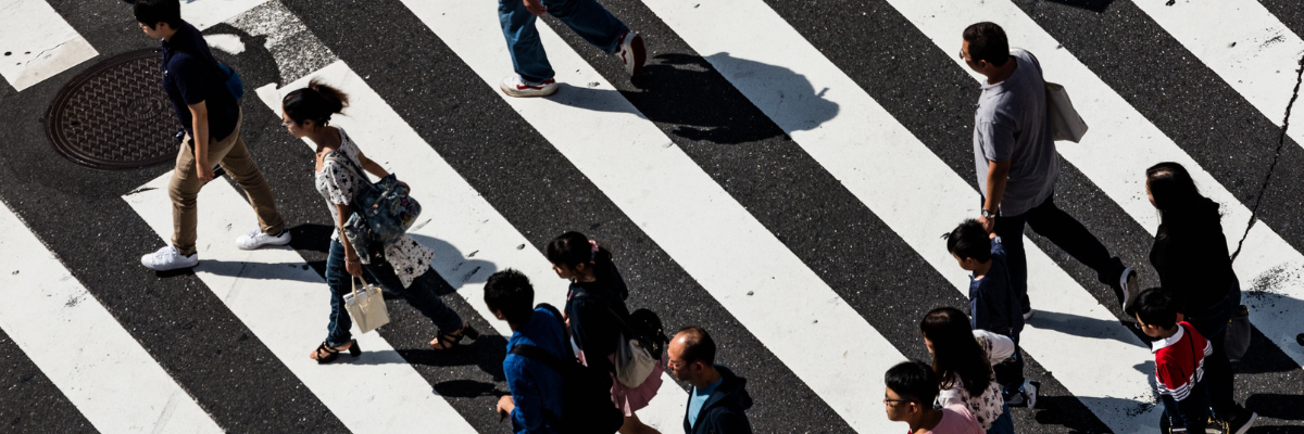 Zdjęcie przedstawia ludzi przechodzących przez pasy na przejściu dla pieszych, widzianych z góry.
